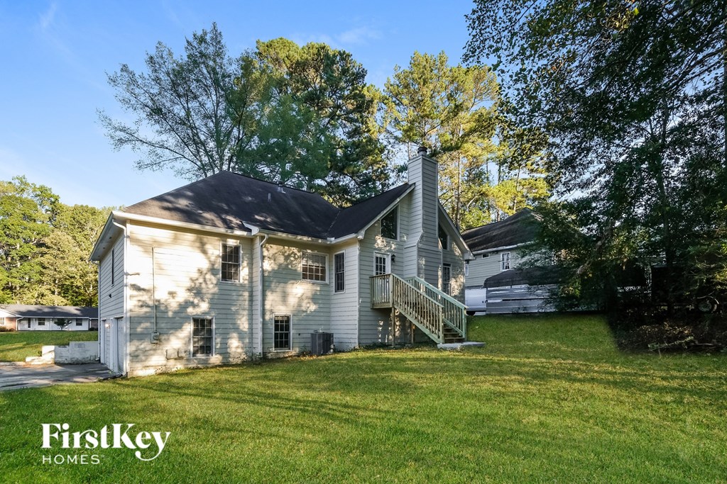 A white house with a black roof and a porch is surrounded by green grass and trees.