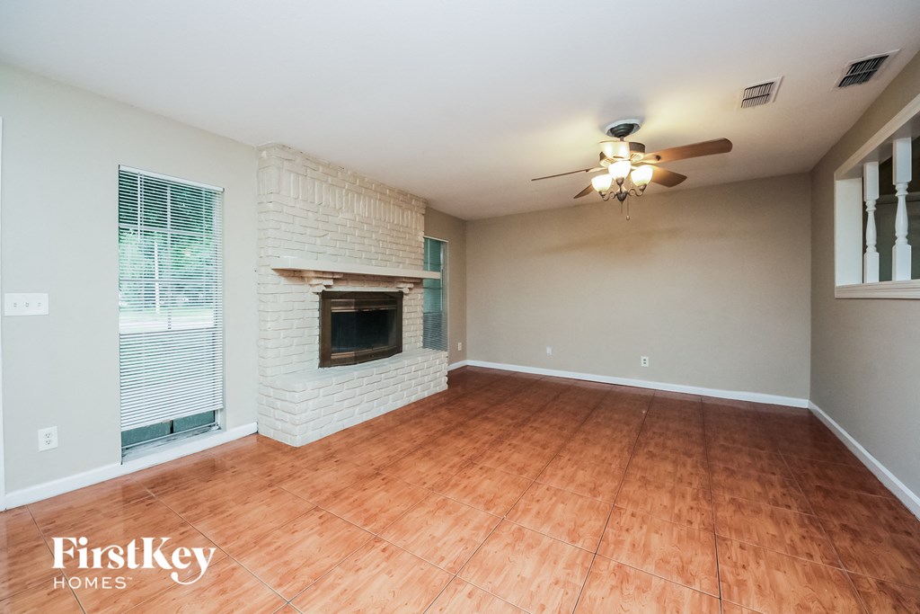 an empty living room with a brick fireplace and a ceiling fan
