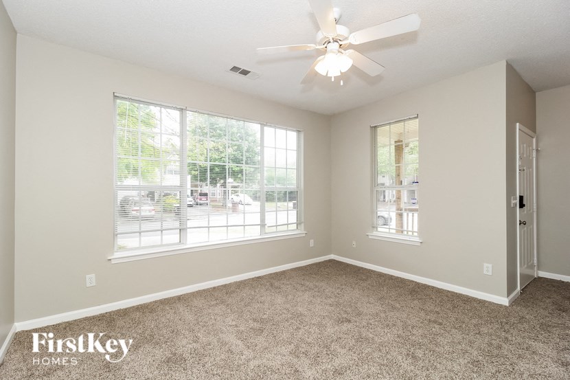 the living room of an empty home with carpet and a ceiling fan