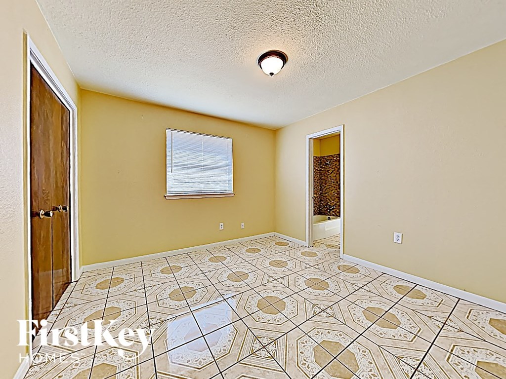an empty living room with a tiled floor and a door to a bathroom