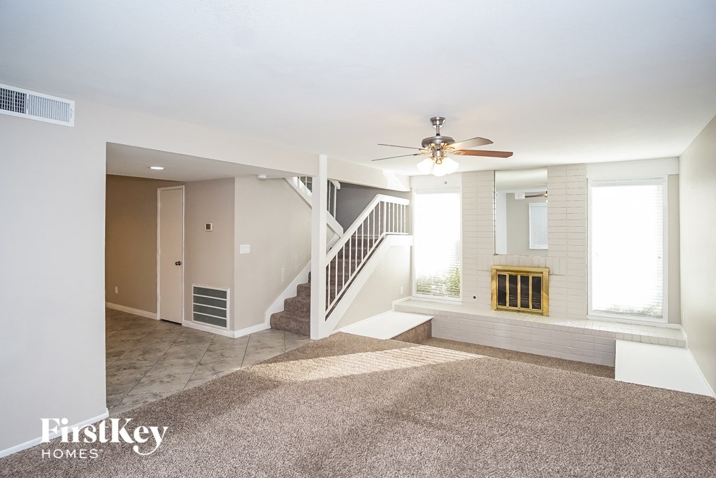 an empty living room with a ceiling fan and a staircase