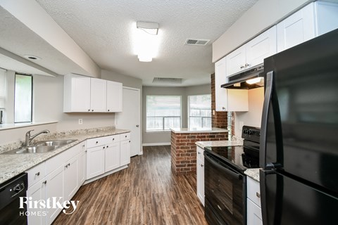 a kitchen with white cabinets and black appliances and a brick wall