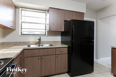 A black refrigerator in a kitchen with wooden cabinets and a granite countertop.