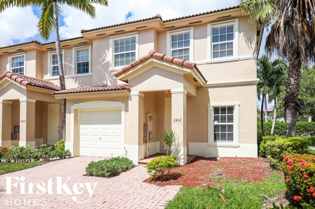 a beige house with a garage and palm trees