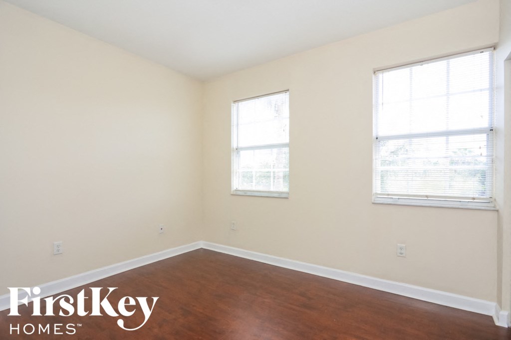 a bedroom with wood floors and two windows