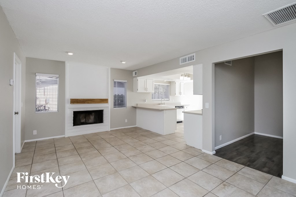 A spacious living room with a fireplace and a kitchen area in the background.