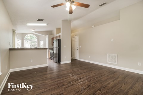 an empty living room with a kitchen and a ceiling fan