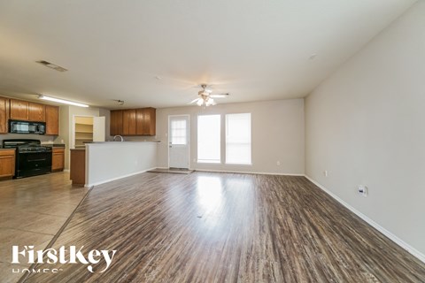 an empty living room with wood flooring and a kitchen