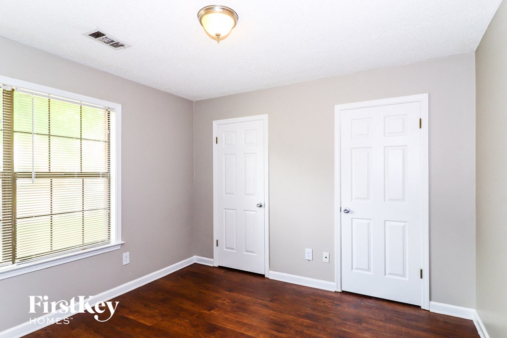 a bedroom with white doors and wood floors and a window