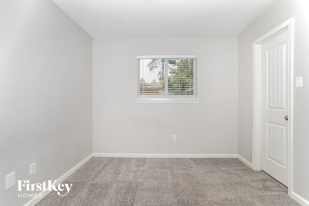 A room with a carpeted floor, a window with blinds, and a door.