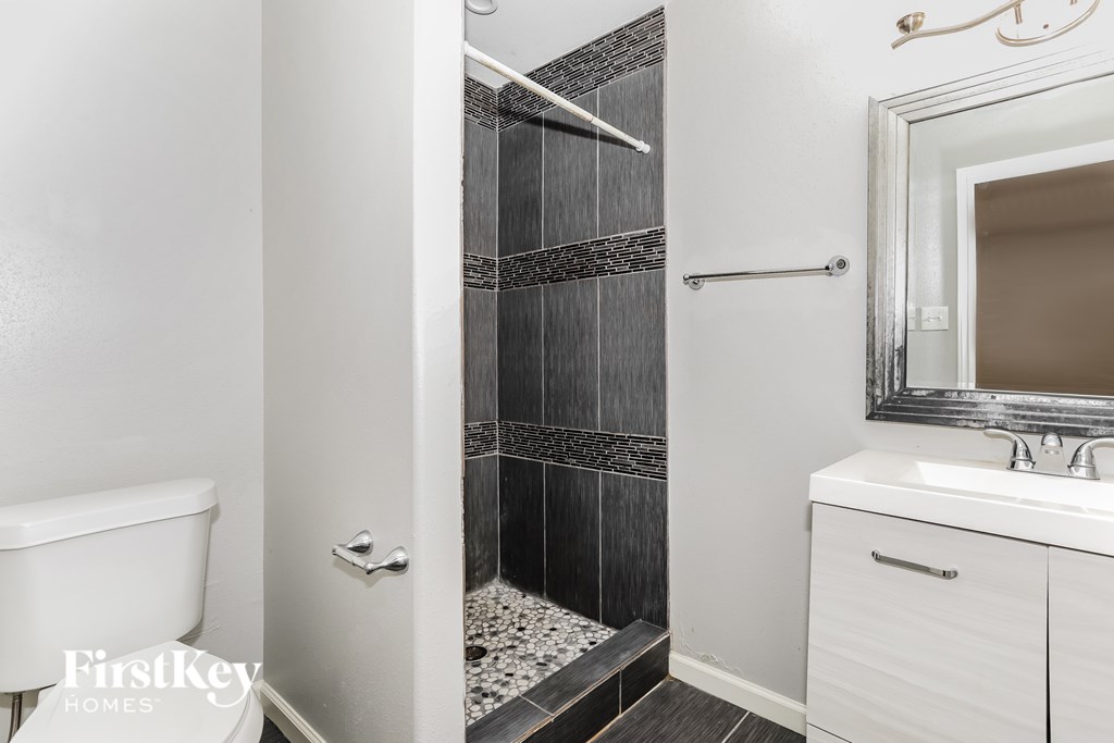 A bathroom with a white toilet, a walk-in shower with a glass door, and a white sink with a mirror above it.