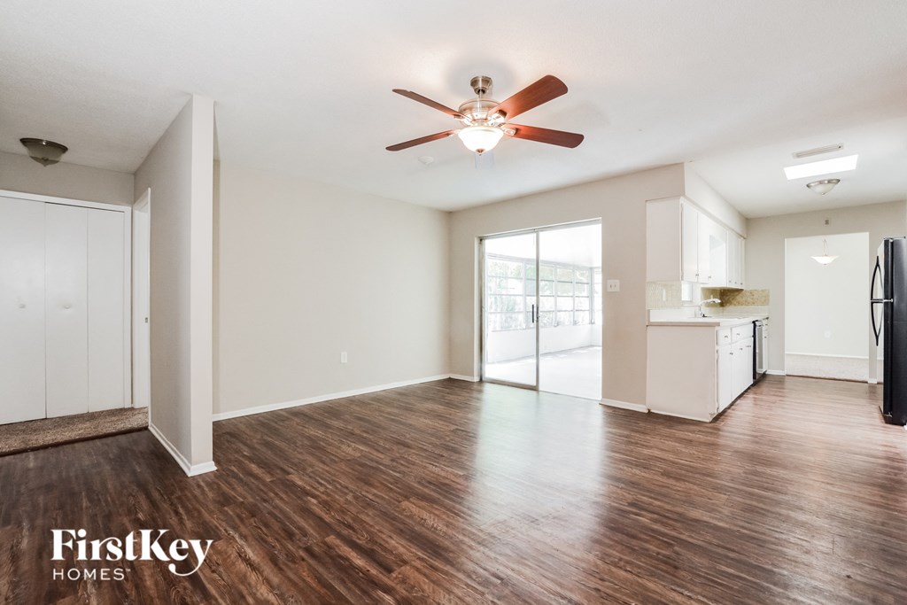 an empty living room with a ceiling fan and a kitchen