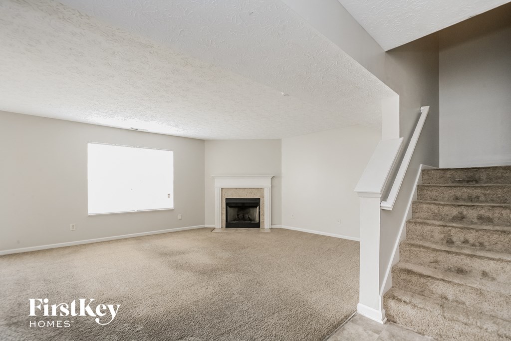 A spacious living room with a fireplace and stairs leading to another level.
