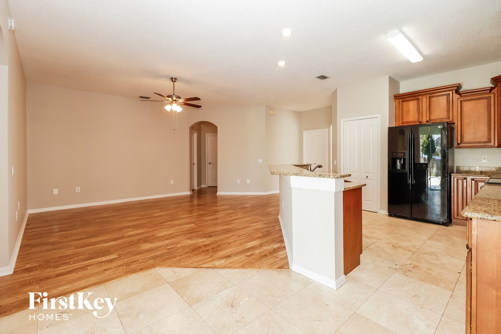 an empty living room with a kitchen and a ceiling fan