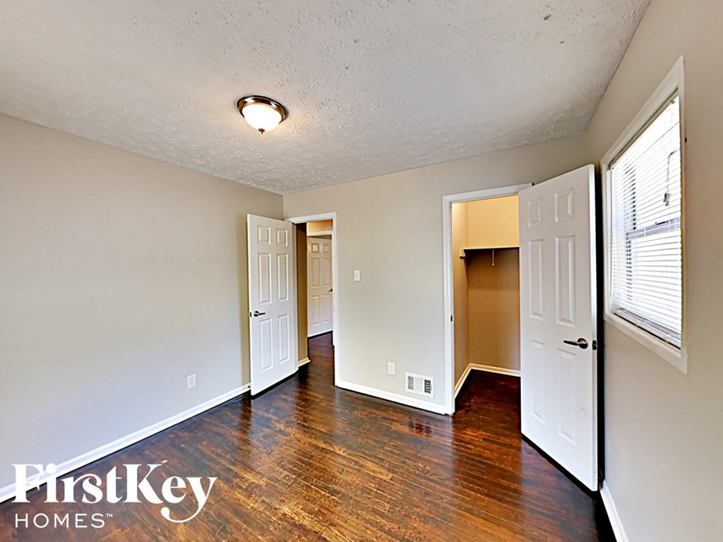 the living room and entrance to a bedroom with wood flooring and a window