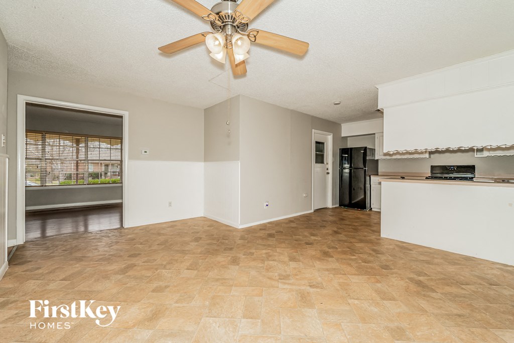 an empty living room with a ceiling fan and a kitchen
