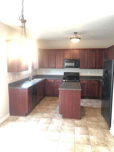 A kitchen with dark wood cabinets and a black refrigerator.