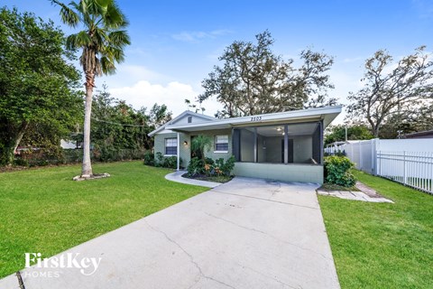 a small blue house with a driveway and a palm tree