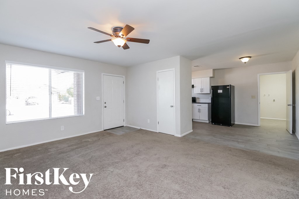 an empty living room with a ceiling fan and a kitchen