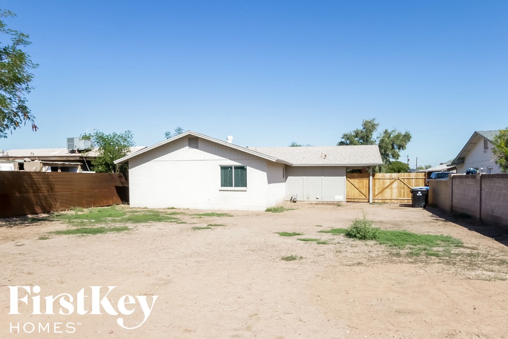 a small white house with a dirt lot and a fence