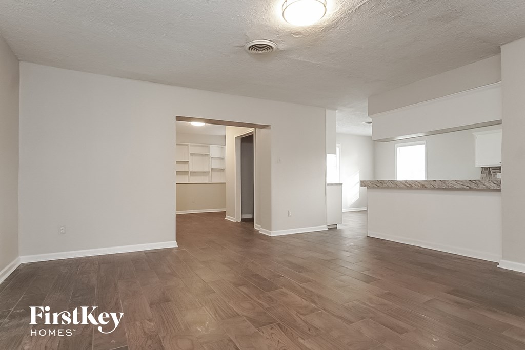 the living room and dining room of an apartment with white walls and wood floors