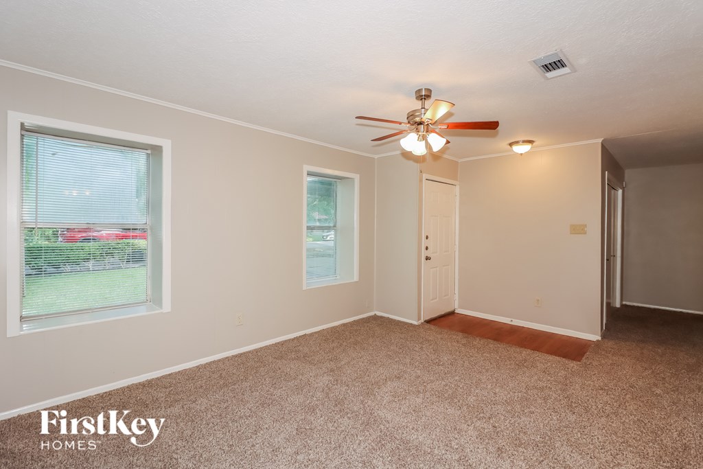 A room with a carpeted floor, a ceiling fan, and a window with blinds.