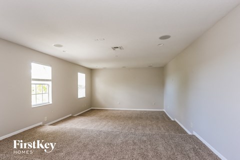 A spacious room with carpeted floor and two windows.