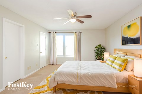 A bedroom with a bed, a ceiling fan, and a painting on the wall.