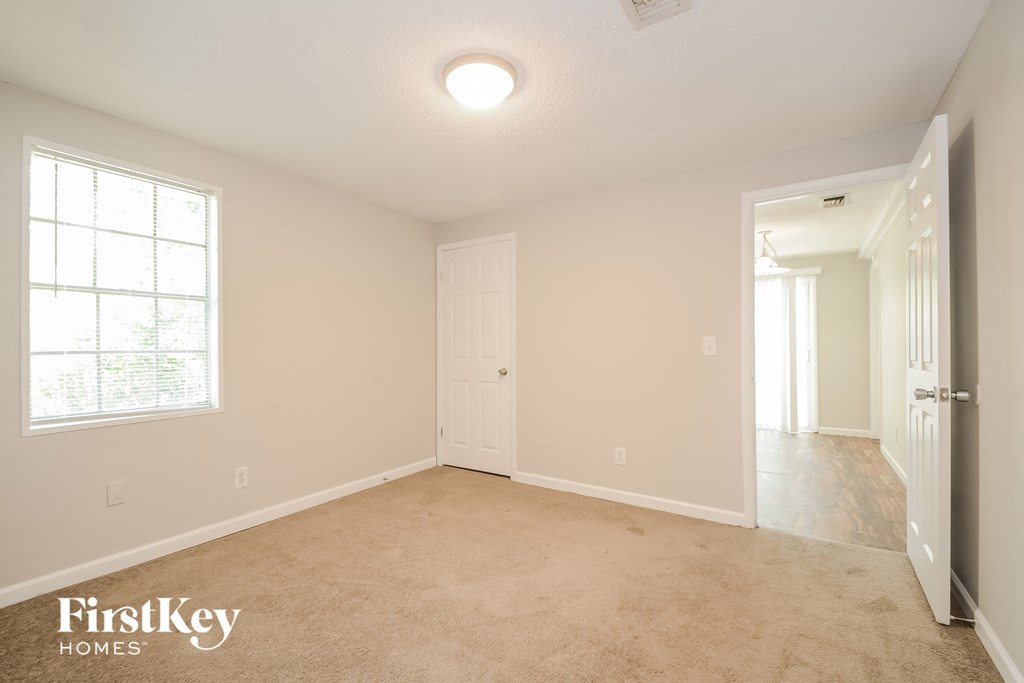 A spacious room with a carpeted floor and a window on the left wall.