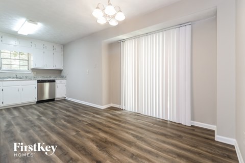 A spacious room with wooden flooring and a kitchen area with white cabinets and a dishwasher.