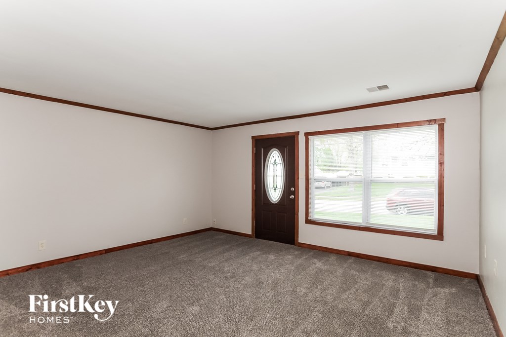 A room with a carpeted floor, a door, and a window showing a red car outside.