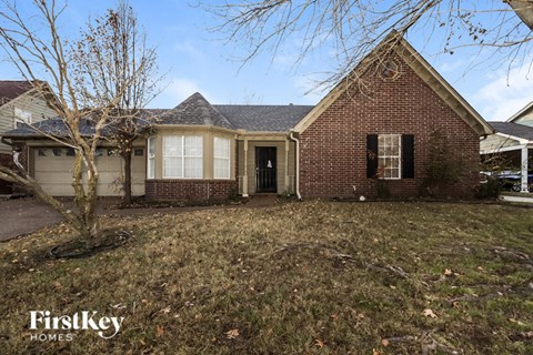 the front of a brick house with a yard and a tree