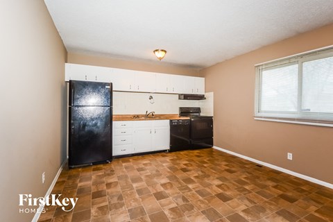 A kitchen with a black fridge, white cabinets, and a brown tiled floor.