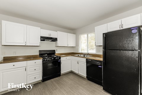 A black refrigerator is in a kitchen with white cabinets.