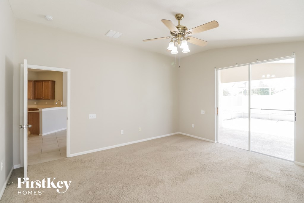 an empty living room with a ceiling fan and a door to the kitchen