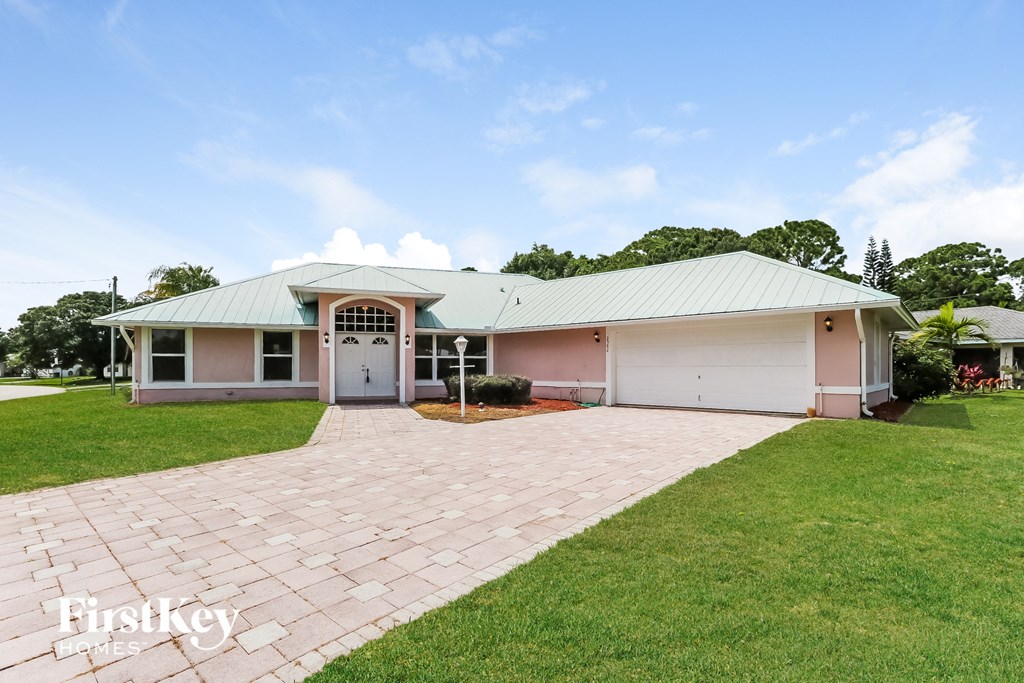 a home with a brick driveway and a white and pink house