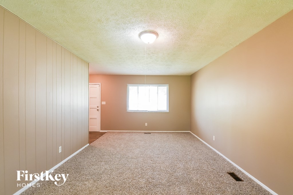 A room with a carpeted floor and a window with white blinds.