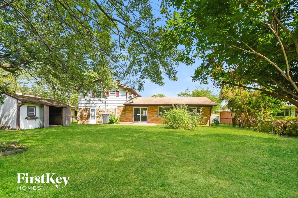 A lush green lawn in front of a house with a tree in the foreground.