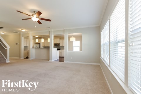 an empty living room with a ceiling fan and large windows