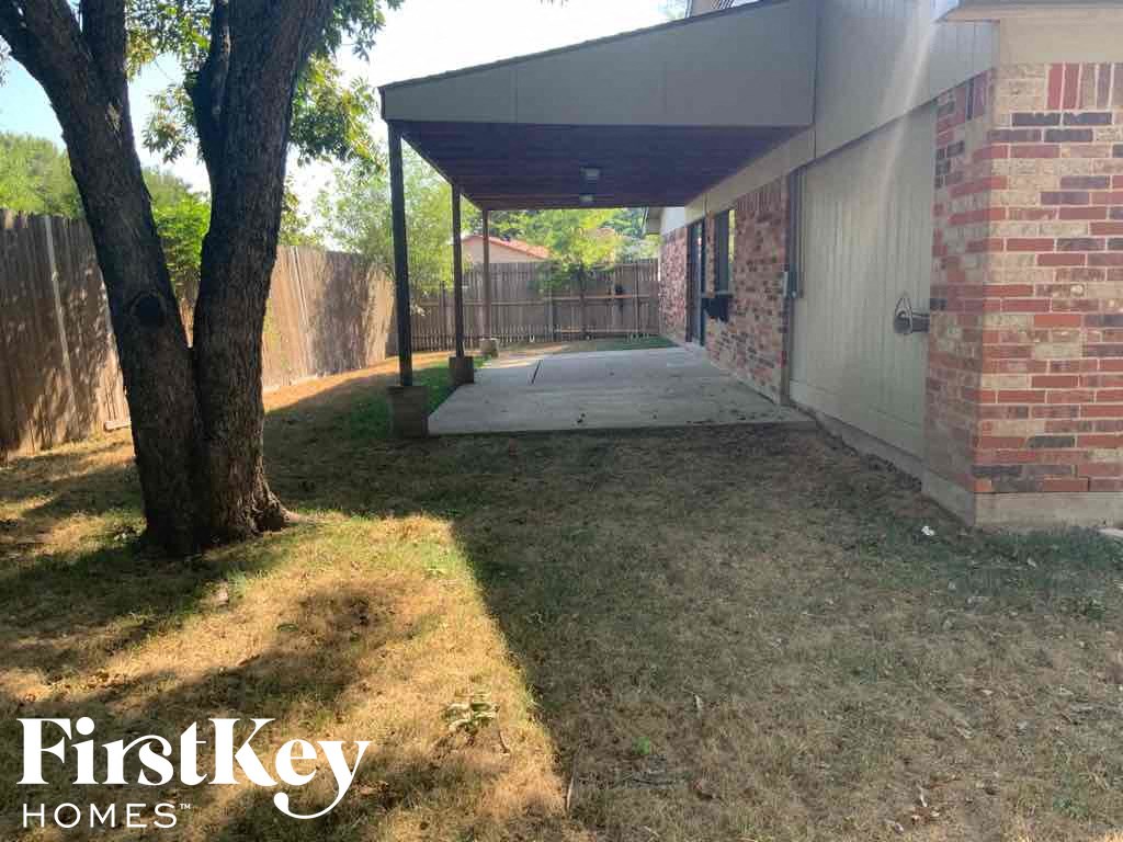 a covered patio in front of a brick house with a tree