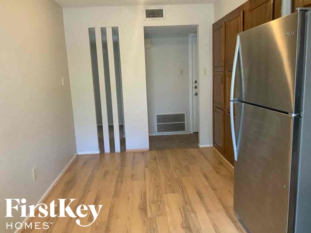 a room with a refrigerator and a hallway with wooden floors