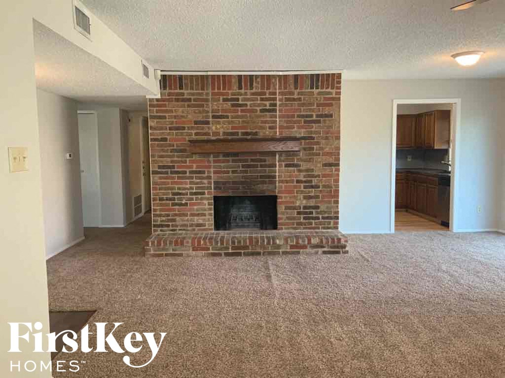 an empty living room with a brick fireplace and a carpeted floor