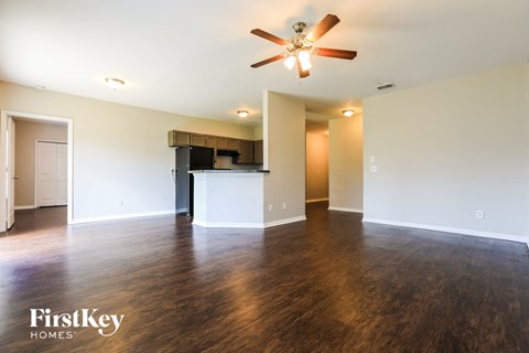 an empty living room with a ceiling fan and a kitchen