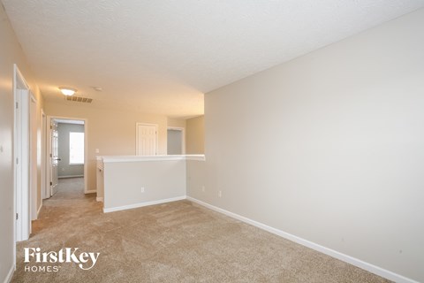 a spacious living room and kitchen with white walls and carpet
