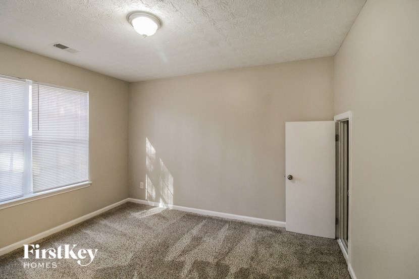 A room with a carpeted floor, a window with blinds, a door, and a FirstKey Homes logo.