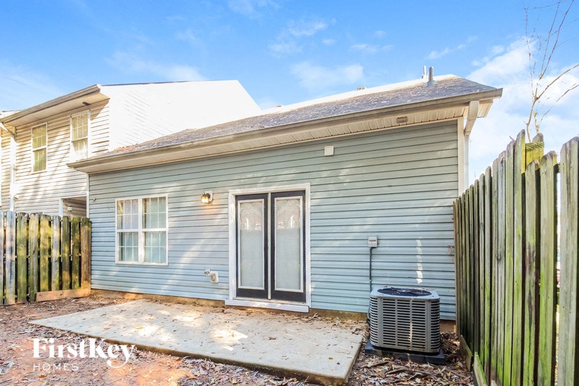 A small house with a grey siding and a white roof is shown with a wooden fence in front.