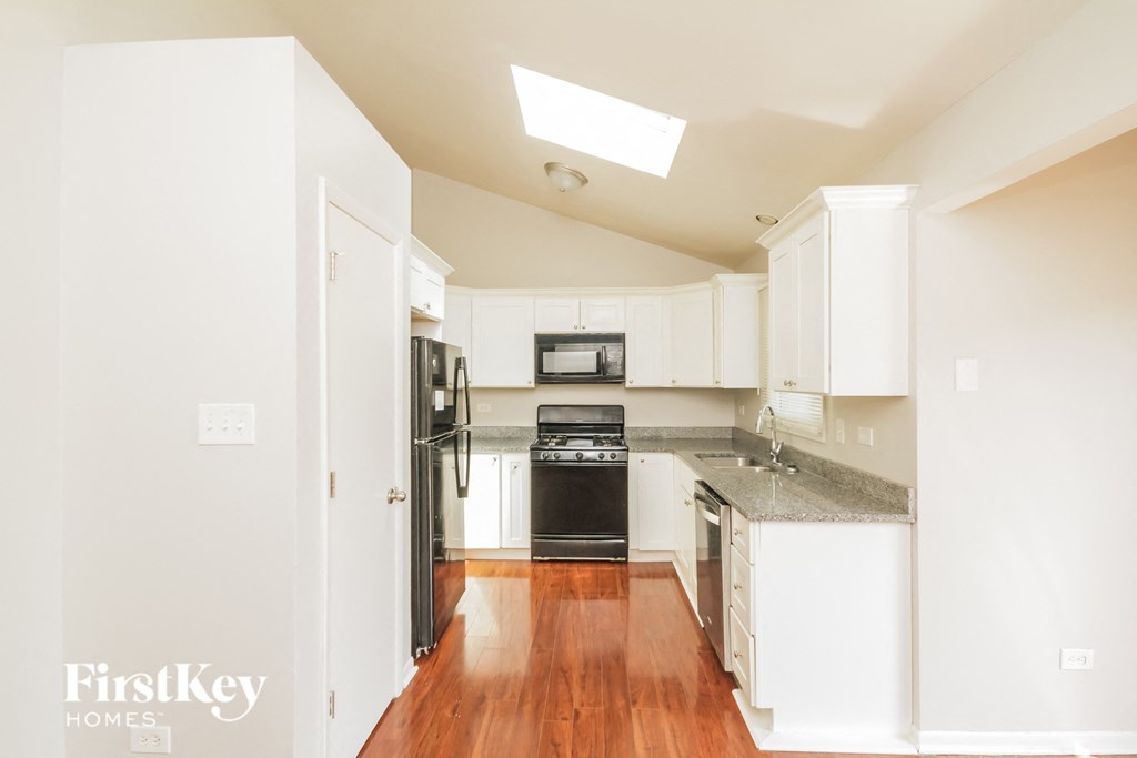 a kitchen with white cabinets and black appliances and a wood floor