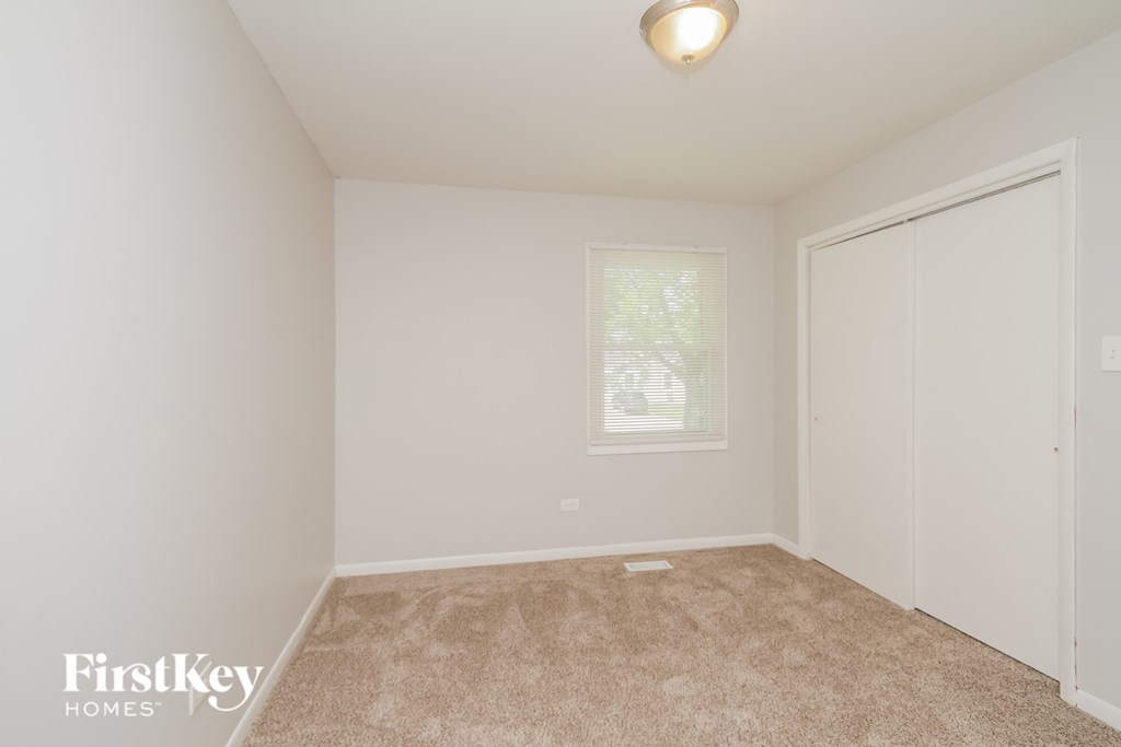 a bedroom with white walls and carpet and a door to a closet