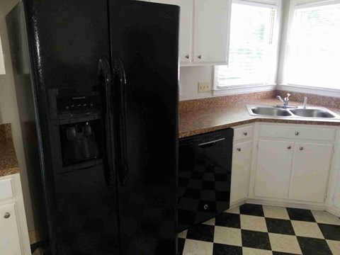 A black refrigerator in a kitchen with checkered floor.