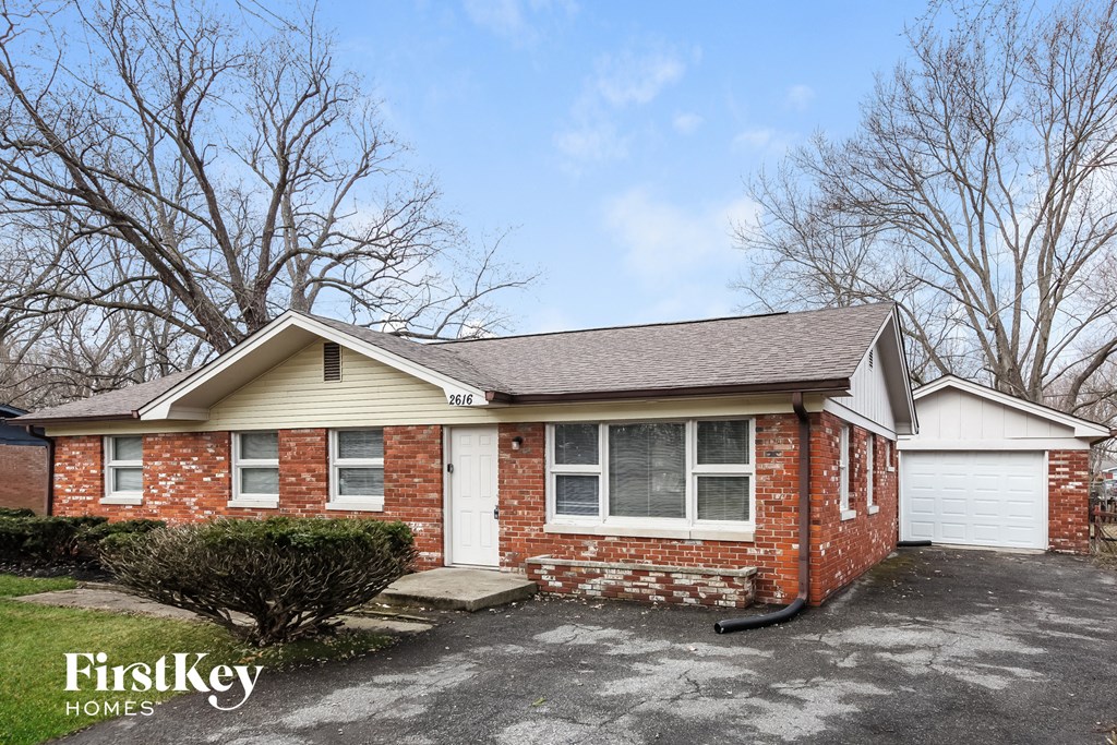the front view of a brick house with a driveway and trees
